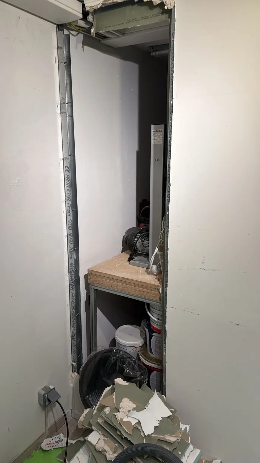 Geöffnete schmale Trockenbauwand mit sichtbarem Kellerraum dahinter